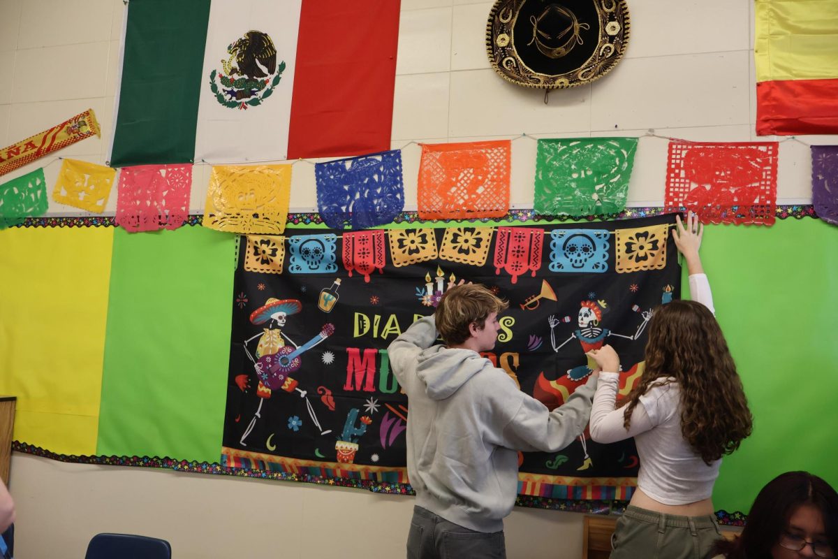 Matthew Adams (‘25) y Brooklyn Ford (‘26) decorando la pared con un tapiz, foto por Anna Wilner.